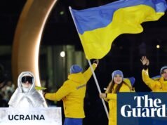 Mulher russa carregando cartaz da seleção ucraniana na cerimônia de abertura dos Jogos Olímpicos de Inverno. Olimpíadas de Inverno de 2026