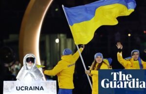 Mulher russa carregando cartaz da seleção ucraniana na cerimônia de abertura dos Jogos Olímpicos de Inverno. Olimpíadas de Inverno de 2026
